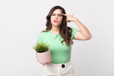 Güzel bir kadın şaşkın ve şaşkın hissediyor, deli olduğunu ve elinde dekoratif bir bitki tuttuğunu gösteriyor.