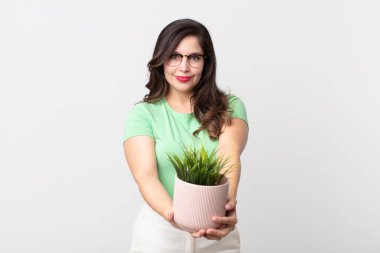 Güzel bir kadın mutlu bir şekilde gülümsüyor ve bir konsept sunuyor ve elinde dekoratif bir bitki tutuyor.
