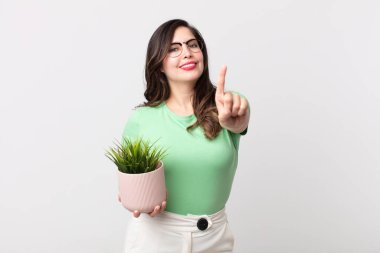 Güzel bir kadın gururla gülümsüyor ve kendine güvenerek bir numara oluyor ve elinde dekoratif bir bitki tutuyor.