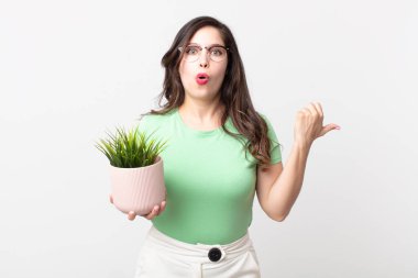 Güzel bir kadın inançsızlıktan şaşkına dönmüş ve elinde dekoratif bir bitki tutuyor.