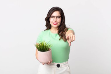 Güzel bir kadın kamerayı işaret ederek seni seçiyor ve elinde dekoratif bir bitki tutuyor.