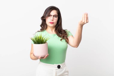 Güzel bir kadın kapiş ya da para hareketi yapıyor, sana ödemeni söylüyor ve elinde dekoratif bir bitki tutuyor.