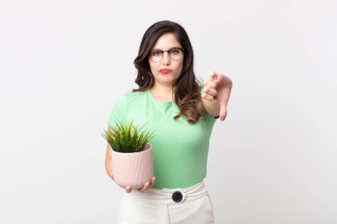 Güzel bir kadın kendini kötü hissediyor, baş parmağını kaldırıyor ve elinde dekoratif bir bitki tutuyor.