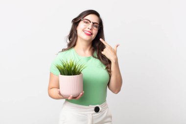 Güzel bir kadın, kendine güvenerek gülümsüyor ve elinde süs bitkisi tutuyor.