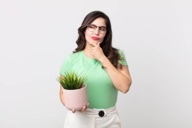 Güzel bir kadın mutlu, kendinden emin bir ifadeyle gülümsüyor. Elleri çenesinde ve elinde dekoratif bir bitki tutuyor.