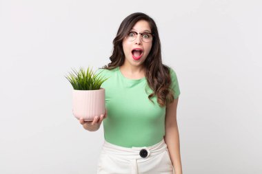 Güzel bir kadın çok şaşırmış ya da şaşırmış görünüyor ve elinde dekoratif bir bitki tutuyor.