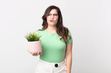 Güzel bir kadın üzgün, üzgün ya da kızgın hissediyor ve elinde dekoratif bir bitki tutuyor.