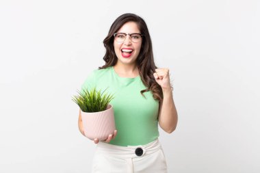 Güzel bir kadın şoke olmuş, gülüyor, başarıyı kutluyor ve elinde dekoratif bir bitki tutuyor.
