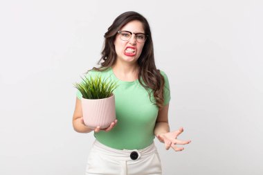 Güzel bir kadın kızgın, sinirli ve hayal kırıklığına uğramış görünüyor ve elinde dekoratif bir bitki tutuyor.
