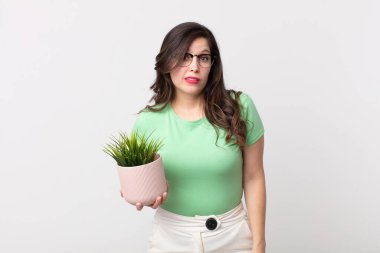Kafası karışmış ve elinde dekoratif bir bitki tutan güzel bir kadın.