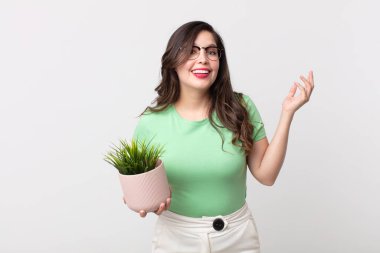 Güzel bir kadın kendini mutlu hisseder, bir çözüm ya da fikir bulduğunda şaşırır ve elinde dekoratif bir bitki tutar.