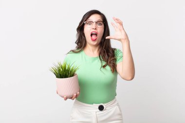 Güzel bir kadın elleri havada bağırıyor ve elinde dekoratif bir bitki tutuyor.
