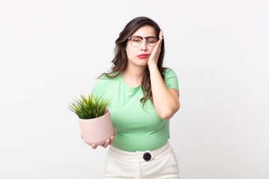 Güzel bir kadın sıkılıyor, hayal kırıklığına uğruyor ve uykulu. Yorucu bir günün ardından elinde dekoratif bir bitki tutuyor.