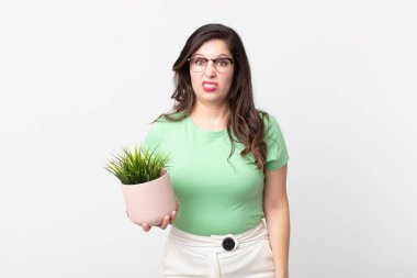 Güzel bir kadın şaşkın ve şaşkın hissediyor ve elinde dekoratif bir bitki tutuyor.