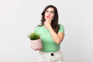 Düşünen, kuşkulu, kafası karışık ve elinde dekoratif bir bitki tutan güzel bir kadın.