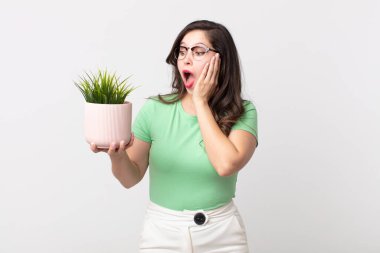 Güzel bir kadın mutlu, heyecanlı ve şaşırmış ve elinde dekoratif bir bitki tutuyor.