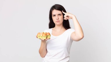 Güzel bir kadın kafası karışık ve şaşkın hissediyor, deli olduğunu ve elinde bir yumurta kutusu tuttuğunu gösteriyor.