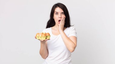 Güzel bir kadın şok olmuş, korkmuş ve elinde bir yumurta kutusu tutuyor.