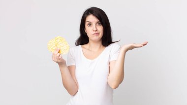 Güzel bir kadın şaşkın, şaşkın ve şüpheci hissediyor ve elinde diyet pirinç keki tutuyor.