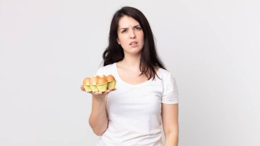 Güzel bir kadın kafası karışmış, kafası karışmış ve elinde bir yumurta kutusu tutuyor.