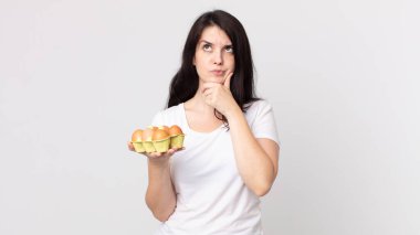 Düşünen, kuşkulu, kafası karışık ve elinde bir yumurta kutusu tutan güzel bir kadın.