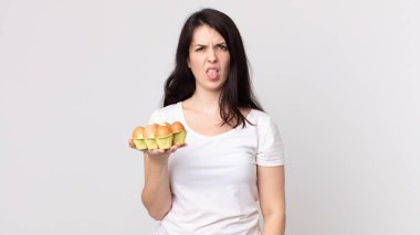 Güzel bir kadın midesi bulanmış ve tedirgin olmuş hissediyor. Dilini çıkarmış ve elinde bir yumurta kutusu tutuyor.