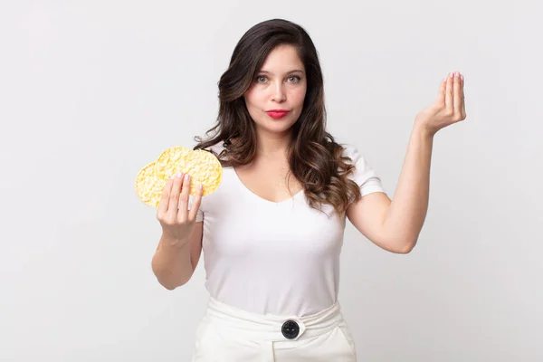 pretty woman making capice or money gesture, telling you to pay and holding a diet rice cakes