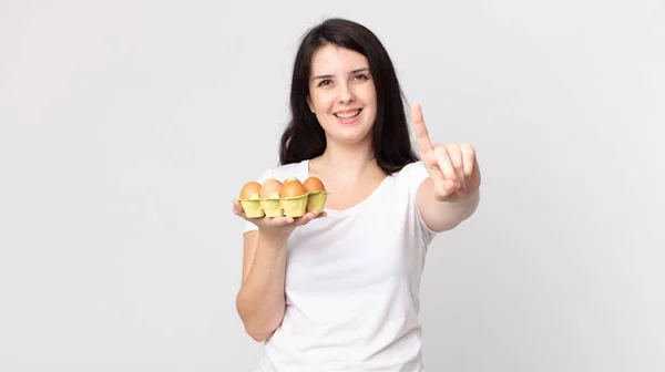 Pretty Woman Smiling Looking Friendly Showing Number One Holding Eggs — Stock Photo, Image