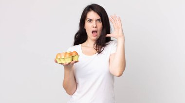 Güzel bir kadın ellerini havaya kaldırıp bağırıyor ve bir yumurta kutusu tutuyor.