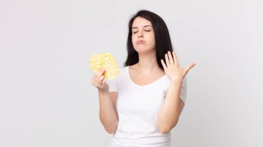 Güzel bir kadın stresli, endişeli, yorgun ve hayal kırıklığına uğramış ve elinde diyet pirinç keki tutuyor.