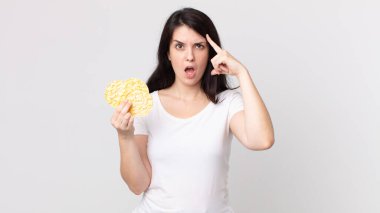 Güzel kadın şaşırmış görünüyor, yeni bir düşünce, fikir ya da konsept fark ediyor ve elinde diyet pirinç keki tutuyor.