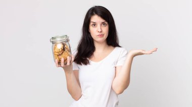 Güzel bir kadın şaşkın, şaşkın, kuşkulu ve elinde cam bir kurabiye şişesi tutuyor.