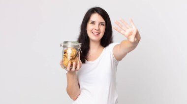 Güzel bir kadın gülümsüyor ve arkadaş canlısı görünüyor. Dört numarayı gösteriyor ve elinde cam bir kurabiye şişesi tutuyor.