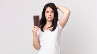 Güzel bir kadın kendini stresli, endişeli ya da korkmuş hissediyor. Elleri başının üstünde ve elinde çikolata tutuyor.