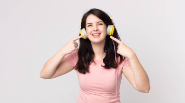 Kendine güvenen güzel bir kadın kendi gülüşünü işaret ederek kulaklıkla müzik dinliyor.