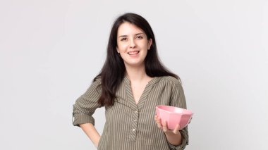 Güzel bir kadın mutlu bir şekilde gülümsüyor, eli kalçasında ve kendine güvenen boş bir tencere tutuyor. Kulaklıklı bir yardımcı ajan.