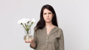 Güzel bir kadın üzgün, üzgün ya da kızgın hissediyor ve bir kenara bakıyor ve elinde dekoratif bir çiçek tutuyor. Kulaklıklı bir yardımcı ajan.