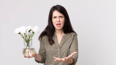 Güzel bir kadın kızgın, sinirli ve hayal kırıklığına uğramış görünüyor ve elinde dekoratif bir çiçek tutuyor. Kulaklıklı bir yardımcı ajan.