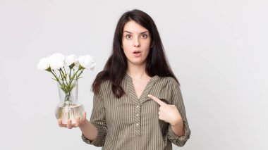 Güzel bir kadın ağzı açık, kendini gösteren ve elinde dekoratif çiçeklerle şok olmuş ve şaşırmış görünüyor. Kulaklıklı bir yardımcı ajan.