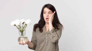 Güzel bir kadın mutlu, heyecanlı ve şaşırmış ve elinde dekoratif bir çiçek tutuyor. Kulaklıklı bir yardımcı ajan.