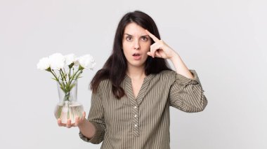Güzel kadın şaşırmış görünüyor, yeni bir düşünce, fikir ya da konsept fark ediyor ve elinde dekoratif bir çiçek tutuyor. Kulaklıklı bir yardımcı ajan.