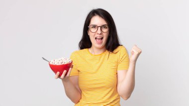 Güzel bir kadın şok geçiriyor, gülüyor, başarıyı kutluyor ve elinde bir kahvaltı kasesi tutuyor.