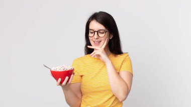 Güzel bir kadın mutlu bir şekilde gülümsüyor ve hayal kuruyor ya da şüphe ediyor ve elinde bir kahvaltı kasesi tutuyor.