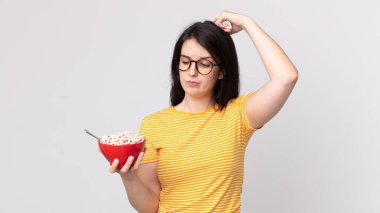 Güzel bir kadın şaşkın ve kafası karışmış hissediyor, kafasını kaşıyor ve elinde bir kahvaltı kasesi tutuyor.