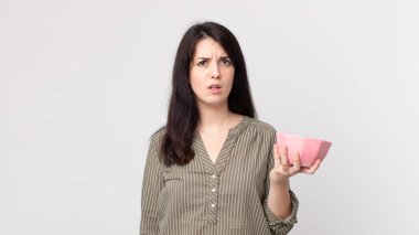 Güzel kadın kafası karışık ve kafası karışmış bir şekilde elinde boş bir tencere tutuyor. Kulaklıklı bir yardımcı ajan.