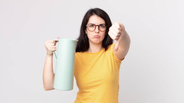 Güzel bir kadın kendini kötü hissediyor, baş parmaklarını gösteriyor ve elinde kahve termosu tutuyor.
