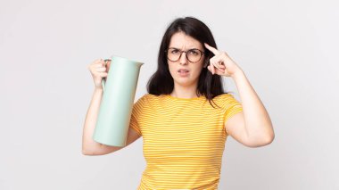 Güzel bir kadın kafası karışık ve şaşkın hissediyor, deli olduğunu ve elinde kahve termosu tuttuğunu gösteriyor.