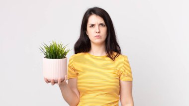 Güzel bir kadın üzgün, üzgün ya da kızgın hissediyor ve elinde dekoratif bir bitki tutuyor.