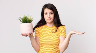 Güzel bir kadın şaşkın, şaşkın, şüpheci ve elinde dekoratif bir bitki tutuyor.