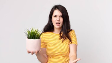 Güzel bir kadın kızgın, sinirli ve hayal kırıklığına uğramış görünüyor ve elinde dekoratif bir bitki tutuyor.